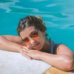 Smiling woman with sunglasses relaxing by a pool on a sunny day.
